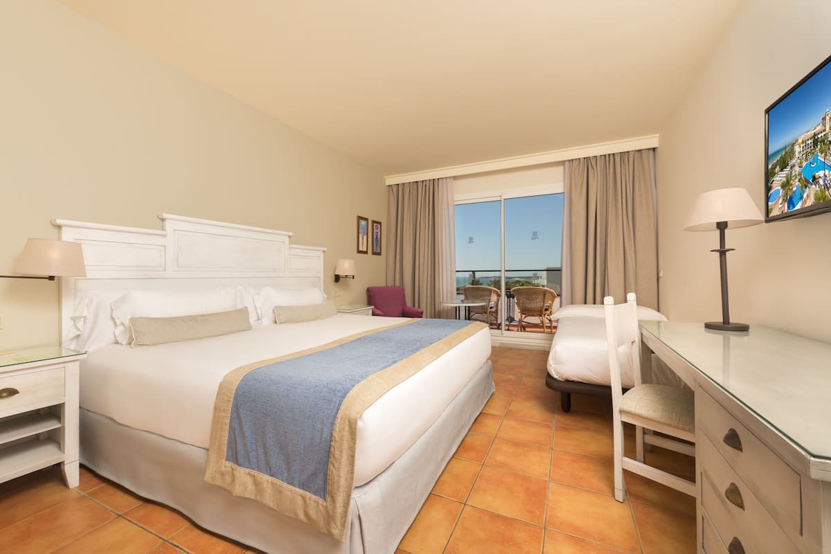 A hotel room with a large bed, a desk, a chair, and a view of the outdoors.