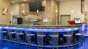 Uma área de bar com balcão, banquetas, prateleiras com garrafas e uma TV de tela plana na parede.
