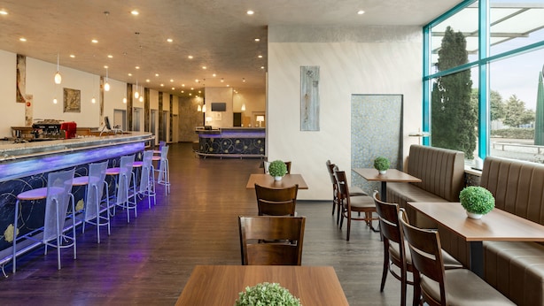 Um restaurante moderno com área de bar, disposição de mesas e amplas janelas com vista.