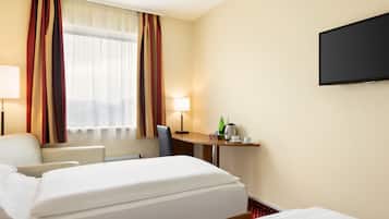 Habitación de hotel con cama, escritorio con lámpara, una silla y televisor.