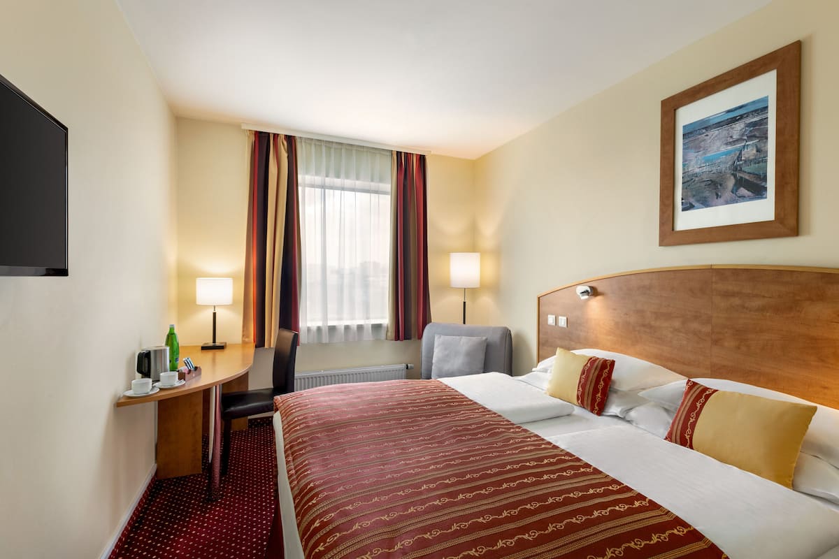 Una habitación de hotel con una cama, un escritorio con silla, un televisor y una ventana con cortinas.