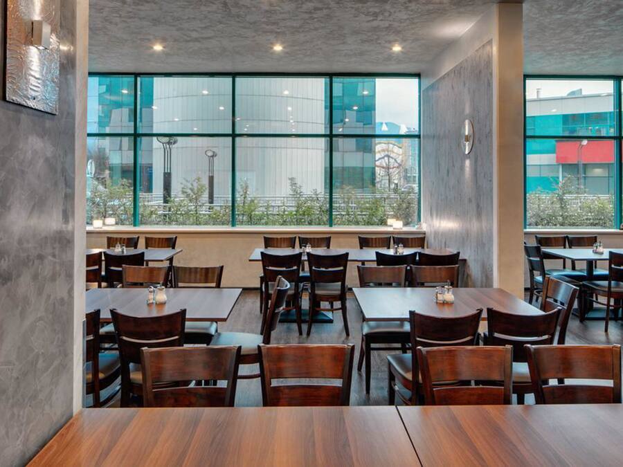 A restaurant with multiple tables and chairs, large windows with a view of buildings, and a modern interior design.