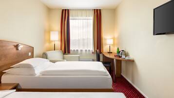 A hotel room with a bed, a desk, a chair, a TV, and a window with curtains.
