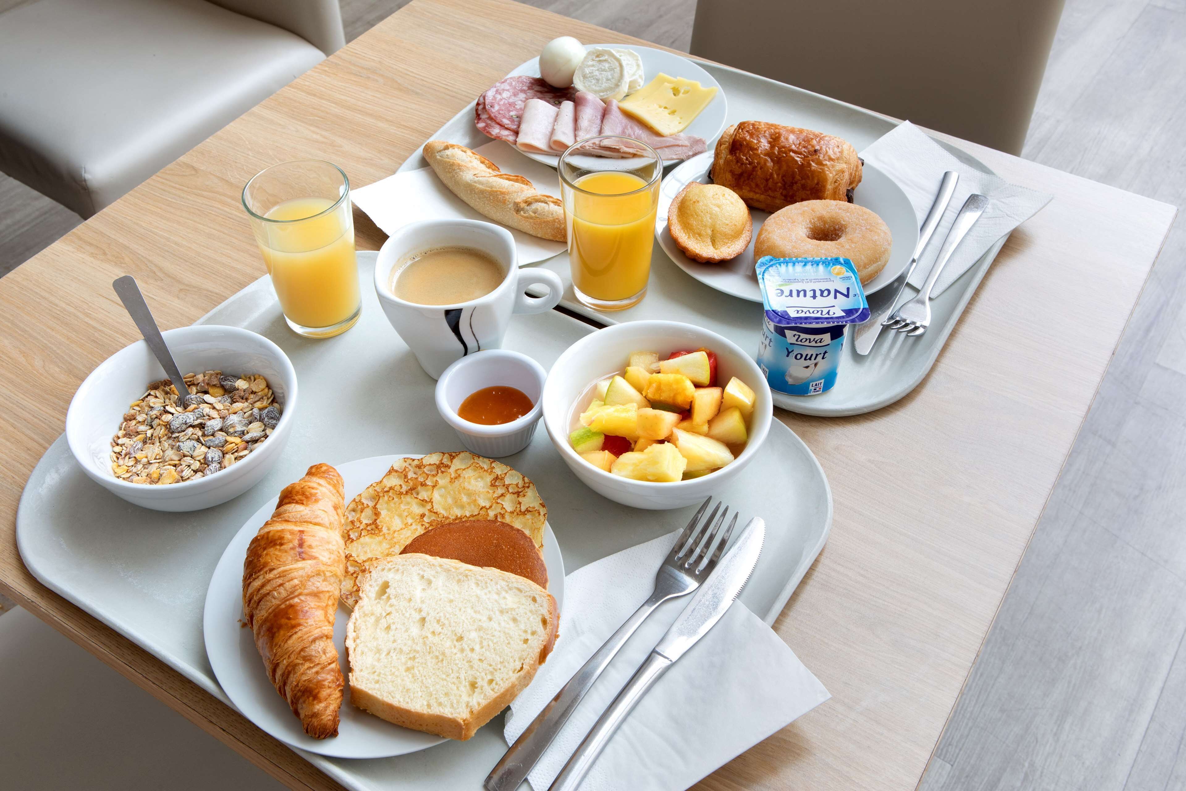 Bandeja de desayuno con cruasanes, pan, fruta, queso, jamón y jugo.