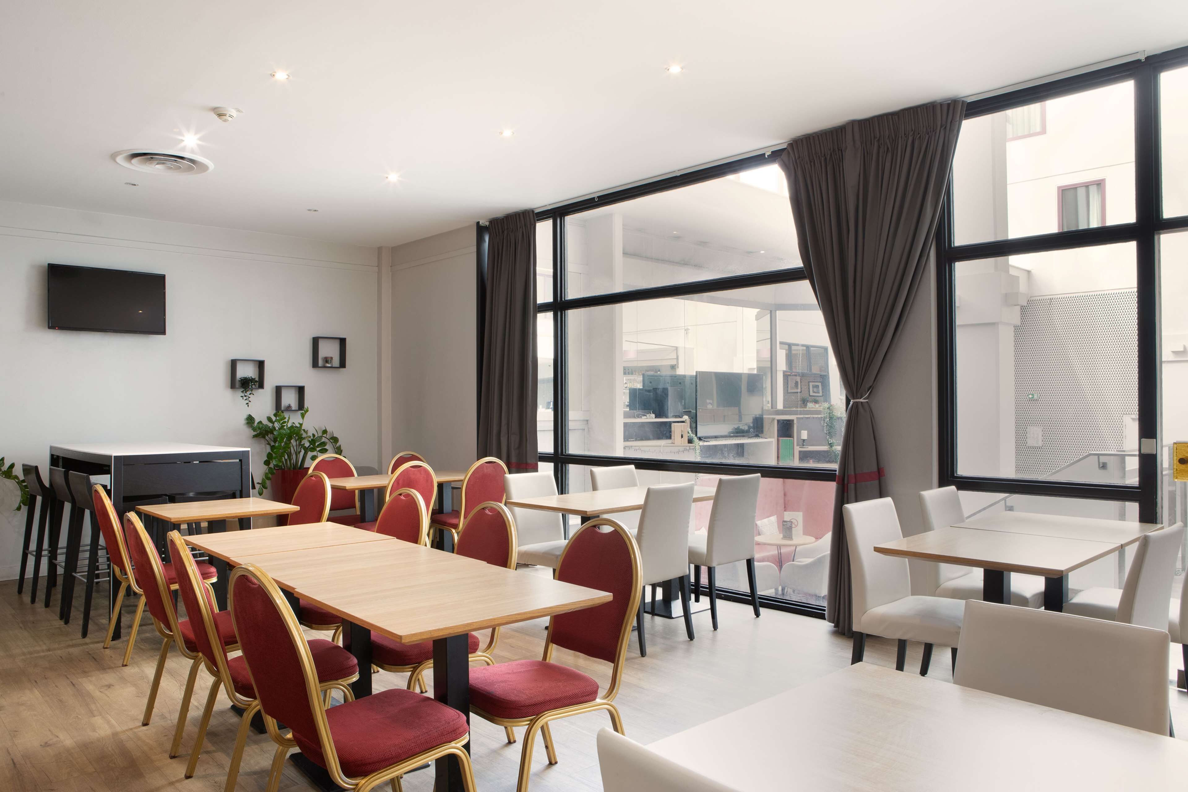 A modern conference room with a large table and chairs, large windows with curtains, and a flat-screen TV on the wall.