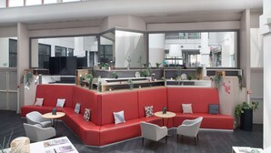 Ein stilvoller Lounge-Bereich mit roten Sitzgelegenheiten, weißen Tischen und großen Fenstern, die einen Blick auf die Stadt ermöglichen.