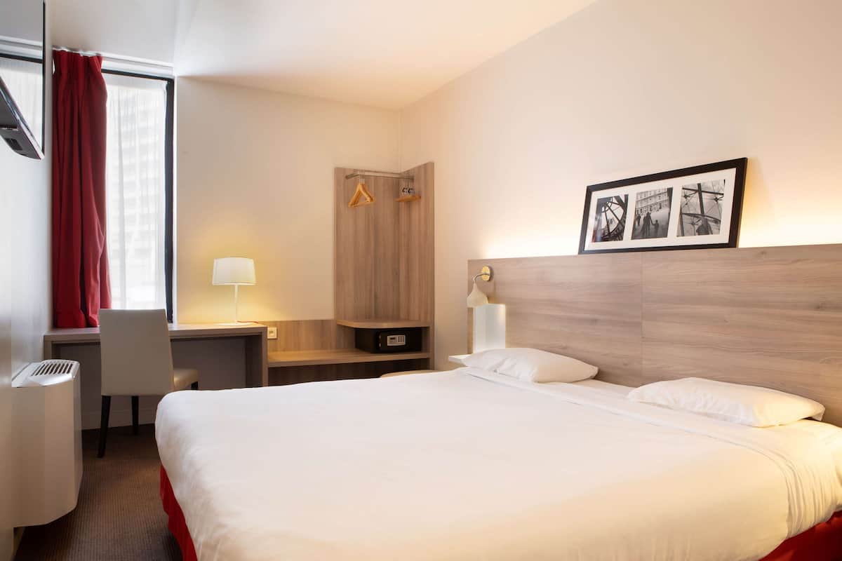 Una habitación de hotel con una cama grande, un escritorio, una silla, un armario y un cuadro en la pared.