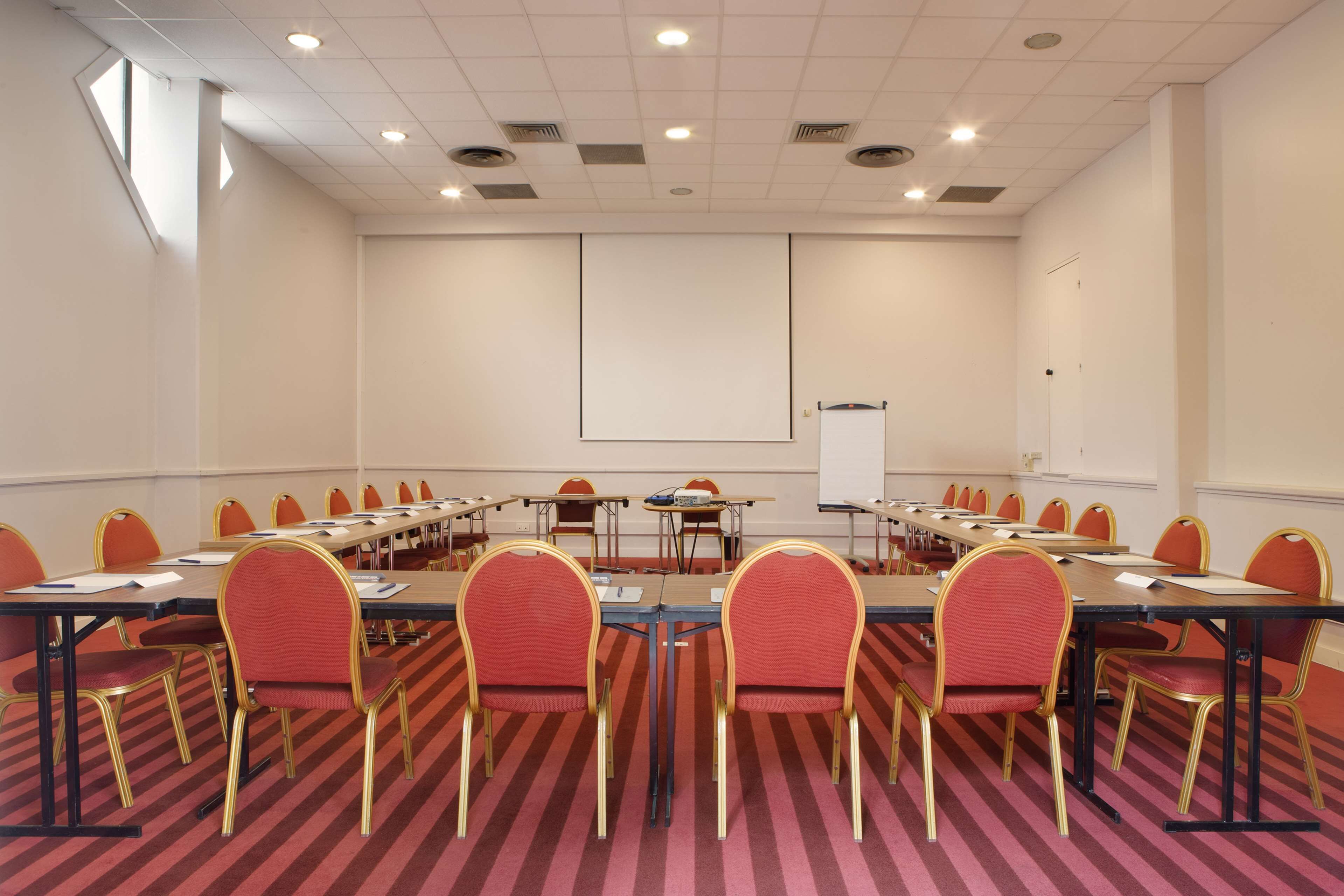 Une salle de conférence avec une longue table, des chaises rouges et un tableau blanc.