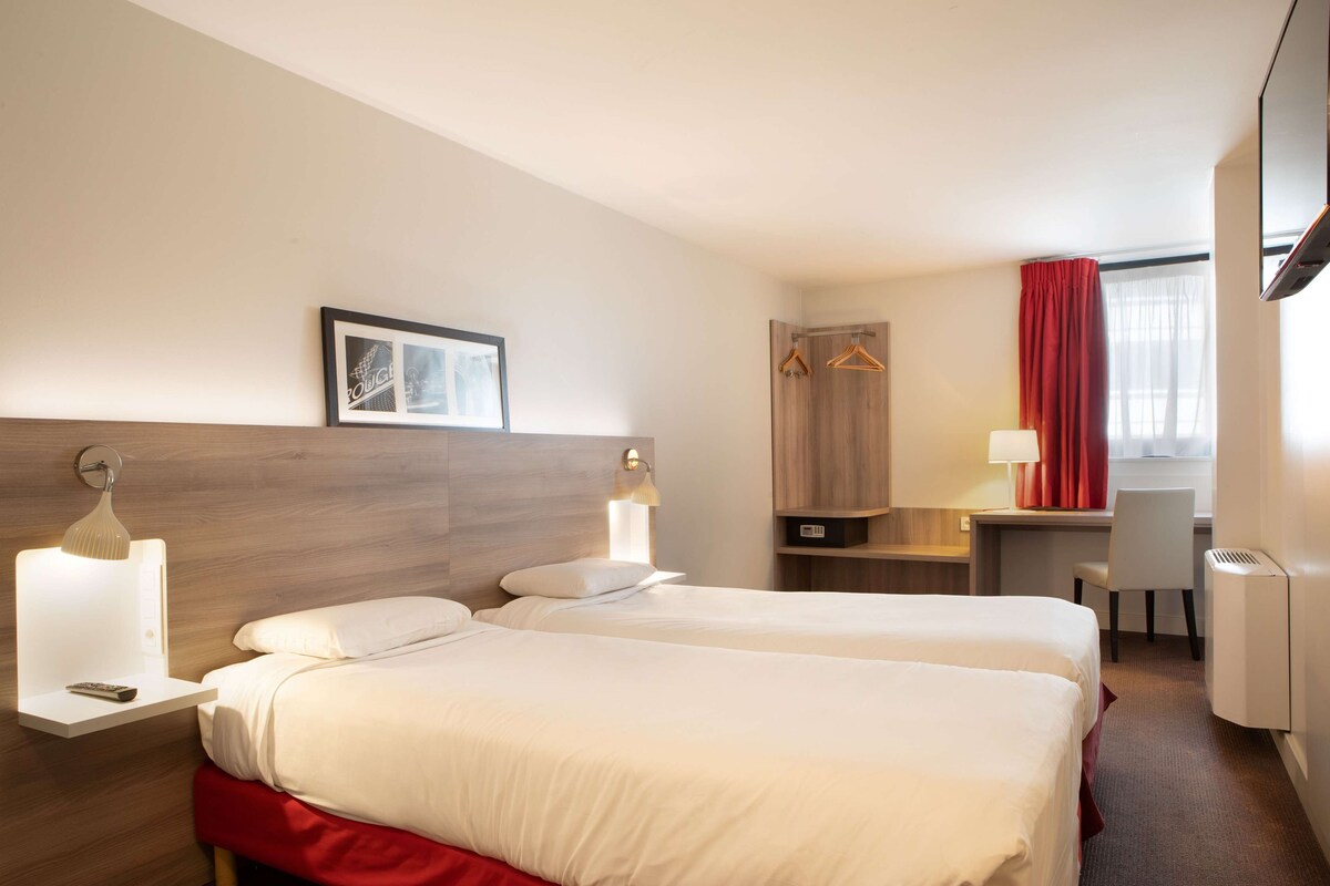 Habitació d'hotel amb dos llits, un escriptori, una cadira, un televisor i una cortina vermella.