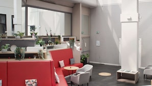 Eine geräumige Lobby mit einer roten Sitzecke, einem weißen Empfangsschalter und großen Fenstern.