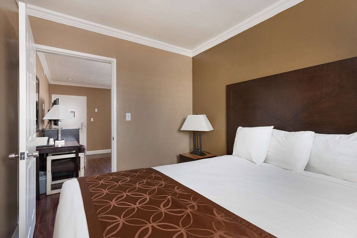 Une chambre d’hôtel avec un grand lit, une table de chevet avec une lampe, un bureau avec une chaise et un miroir.