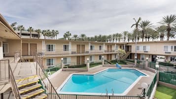 Un hotel de varios pisos con una piscina central, escaleras exteriores y palmeras.