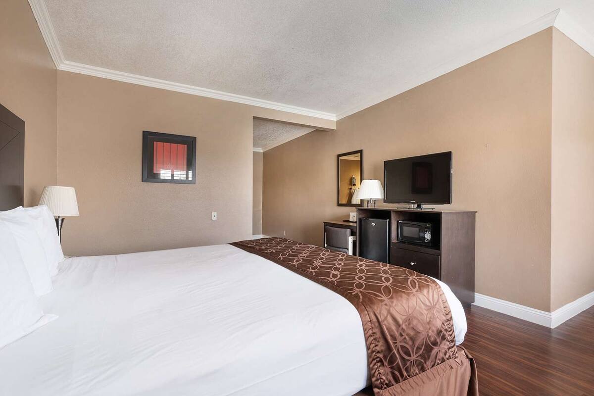 Une chambre d’hôtel avec un grand lit, un bureau avec un ordinateur, une télévision et un four à micro-ondes.