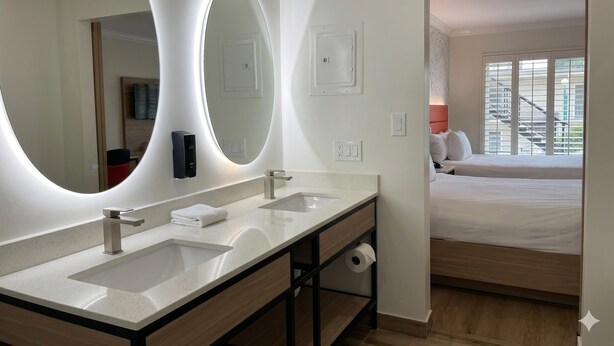 A hotel bathroom with a large mirror, two sinks, a towel dispenser, and a toilet paper holder. - Americas Best Value Inn & Suites Anaheim Convention Center (Anaheim)