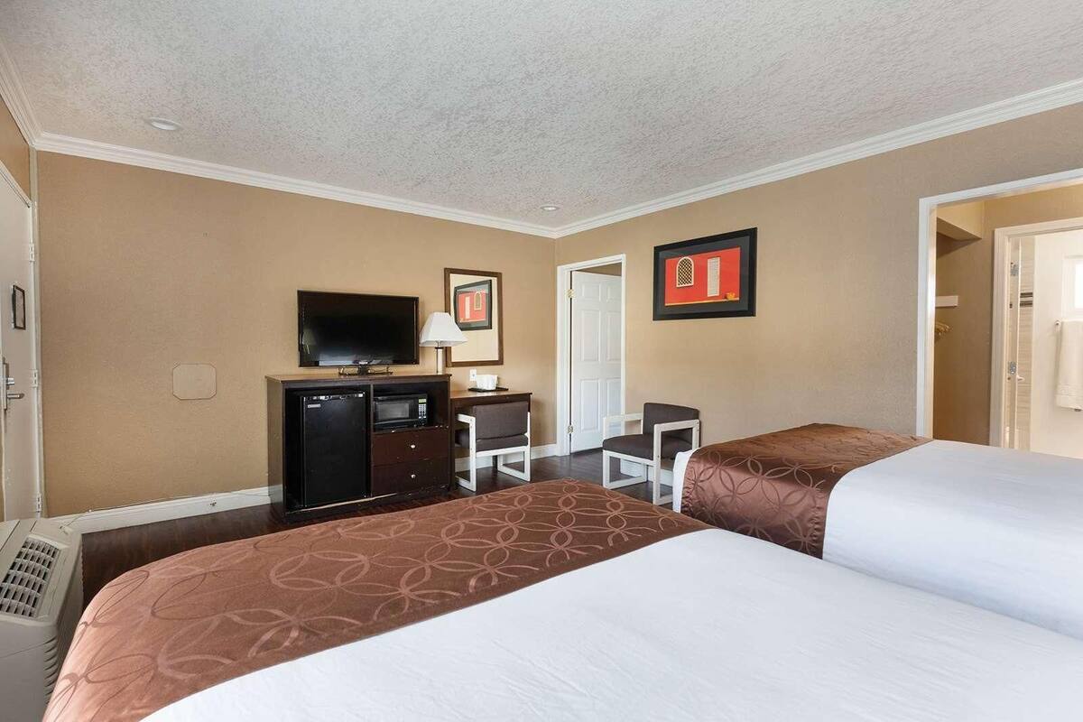Une chambre d’hôtel avec deux lits, un bureau, une télévision, un four à micro-ondes et une porte.