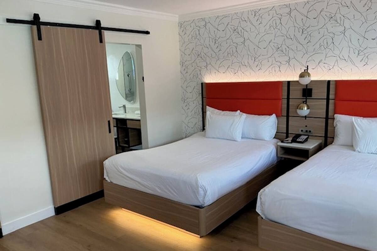 Une chambre d’hôtel avec deux lits, une porte coulissante, une salle de bain avec un miroir et un mur décoré.