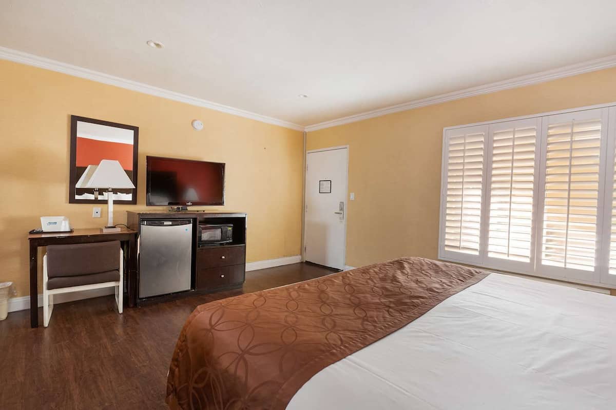 Une chambre d’hôtel équipée d’un lit, d’un bureau, d’un réfrigérateur, d’un four à micro-ondes, d’une télévision et d’une fenêtre avec des stores.