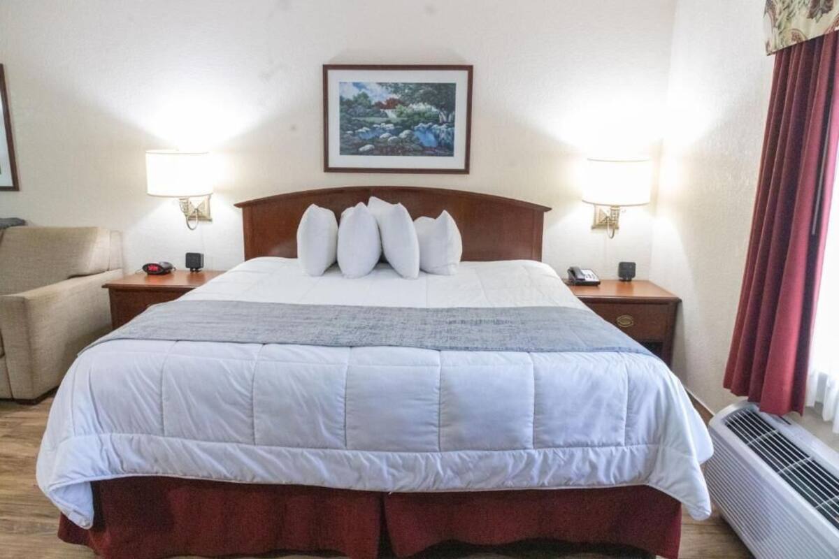 Ein Hotelzimmer mit einem großen Bett, zwei Nachttischlampen, einem gerahmten Bild an der Wand, einem roten Vorhang und einem roten Sofa in der Ecke.