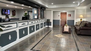 A reception area with a counter, a television, a clock, and a plant. - Homestead Apart-Hotel (Pleasantville)