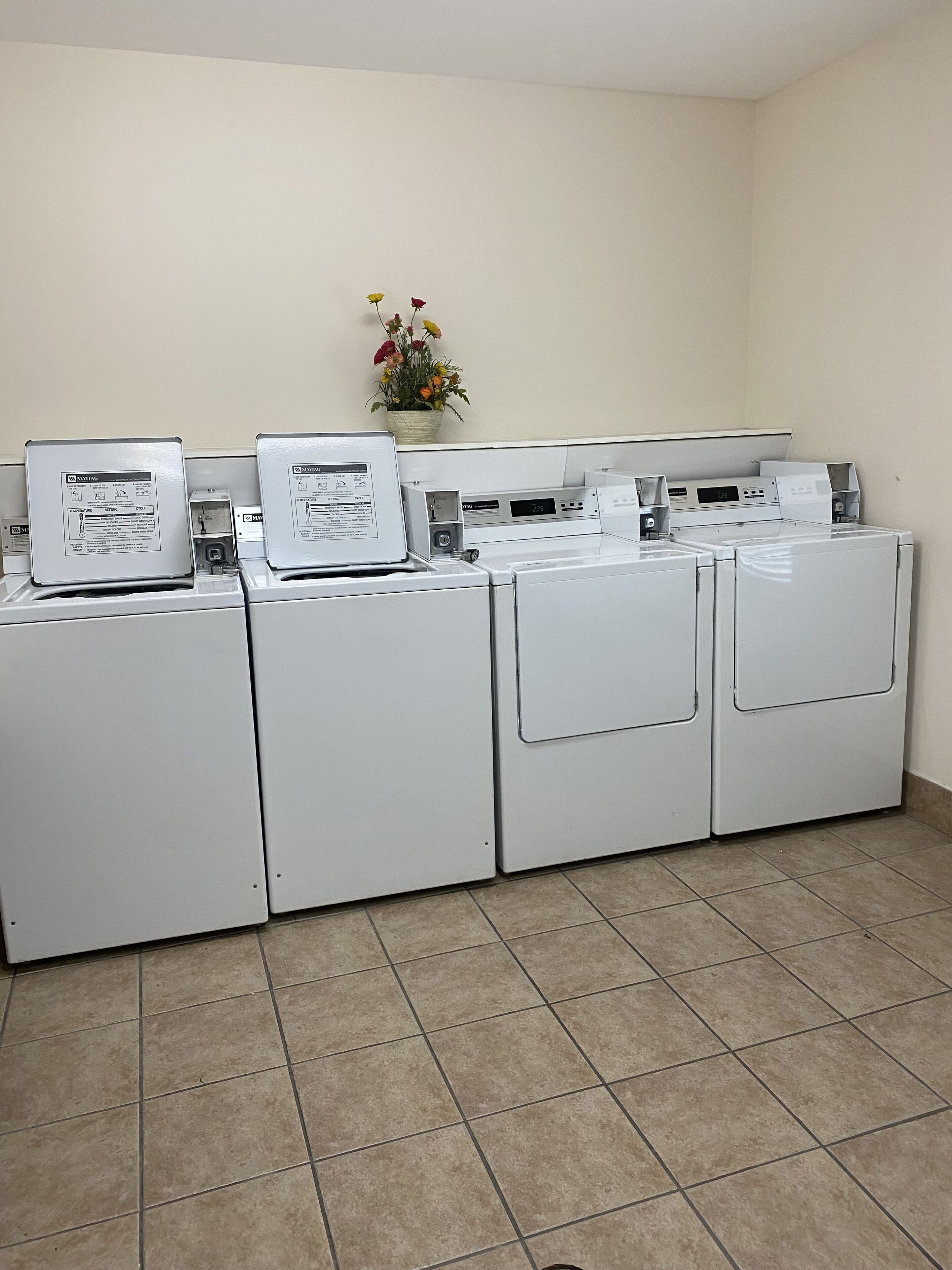 A laundry area with four white washers and dryers, a control panel, and a flower vase on the wall.