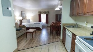 A compact hotel room with a bed, a small sofa, a dining table with chairs, a kitchen area with a sink and stove, and a window with curtains. - Homestead Apart-Hotel (Pleasantville)