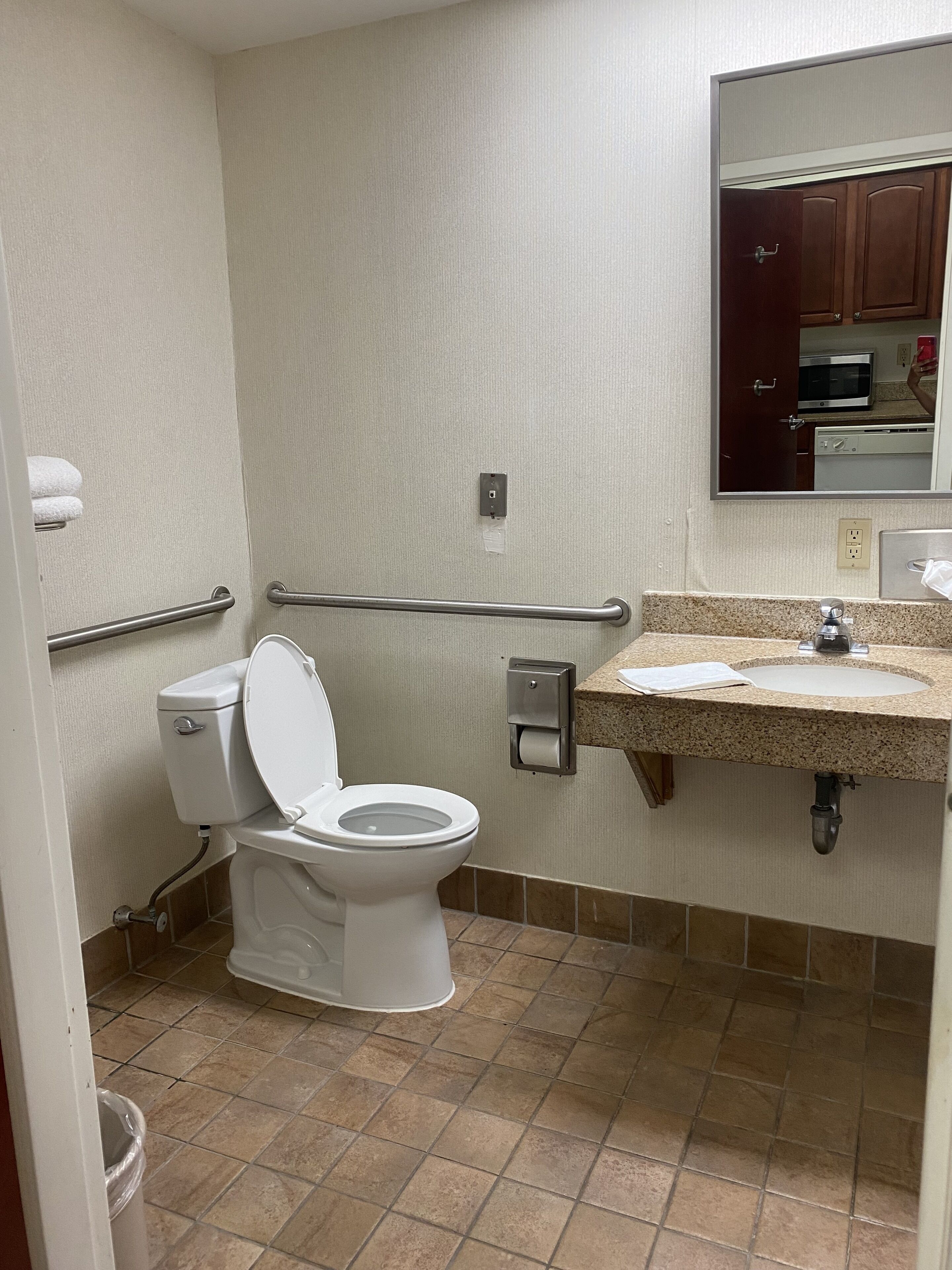 A bathroom with a white toilet, a sink with a paper towel dispenser, and a mirror above the sink.