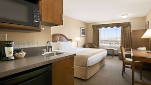 Een hotelkamer met een kitchenette, een bed, een bureau en uitzicht op de stad.