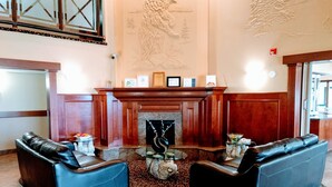 Een hal met twee leren banken, een open haard en een decoratief muurschilderij.