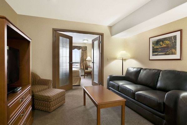 A living room with a leather sofa, a wooden table, a TV stand, and a framed picture on the wall. - Super 8 by Wyndham High Level AB (High Level)