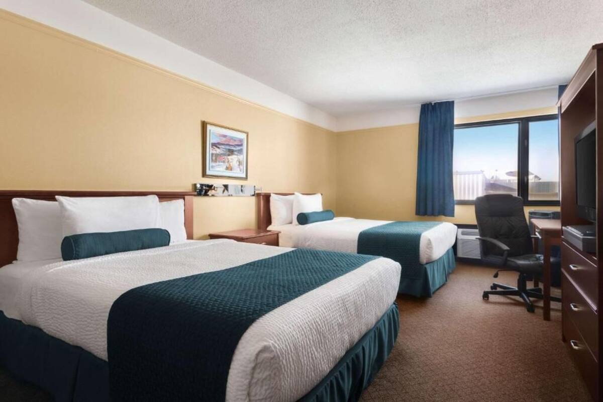 Une chambre d’hôtel avec deux lits, un bureau, une chaise et une grande fenêtre donnant sur un beau paysage.