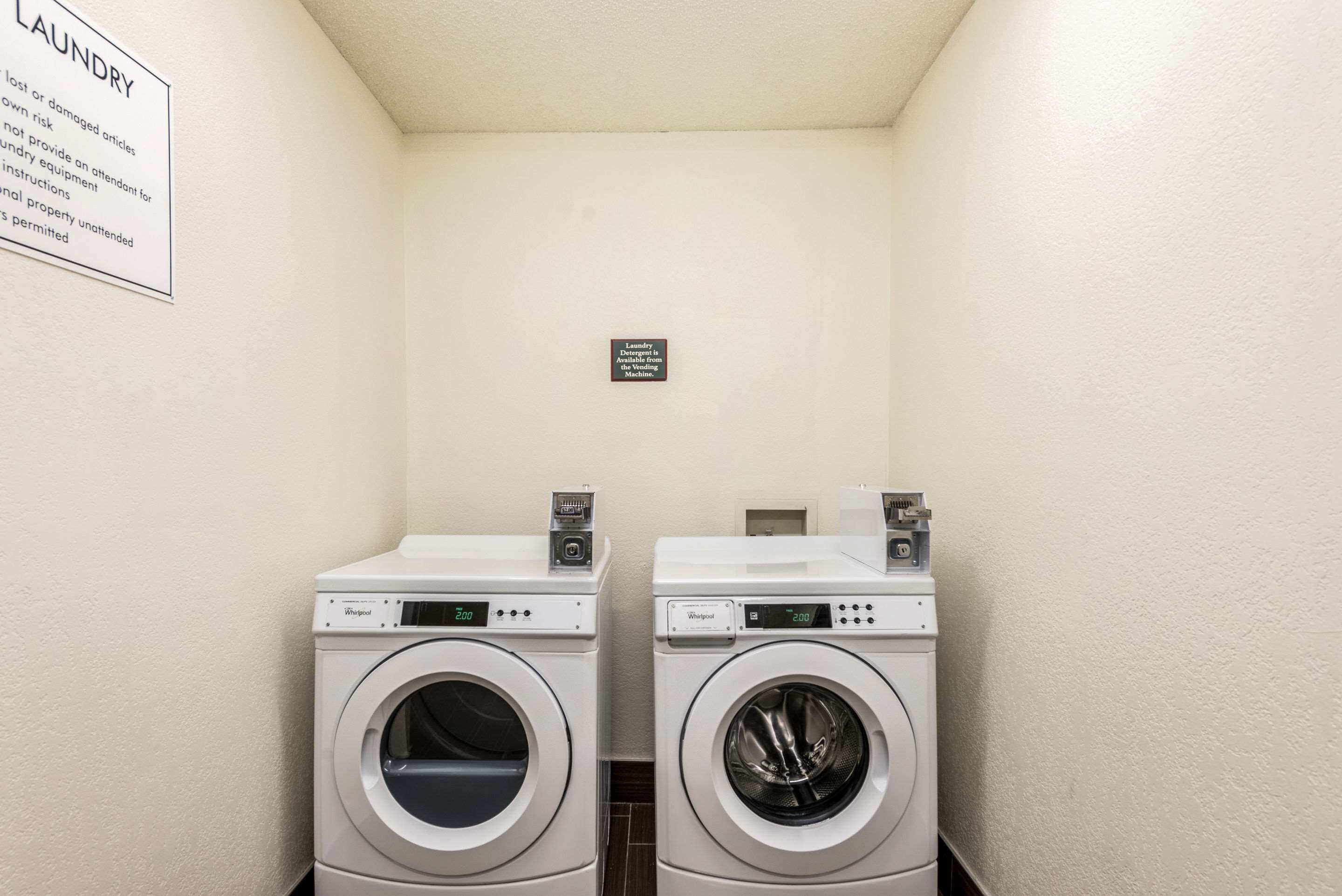 A laundry room with two Whirlpool brand front-loading washers and dryers, a sign indicating laundry detergent is available in vending machines, and a sign warning about lost or damaged articles.