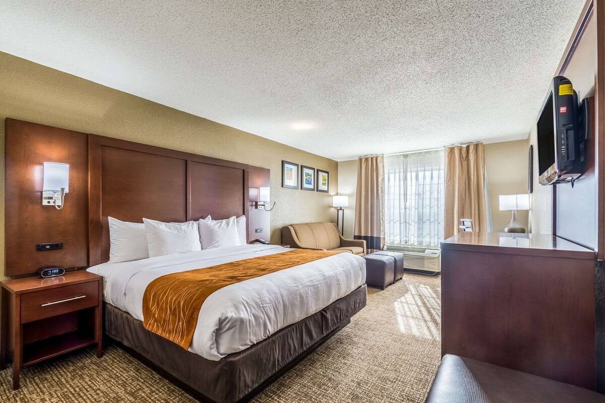 Une chambre d’hôtel avec un grand lit, un bureau, une chaise, une télévision et une fenêtre avec des rideaux.