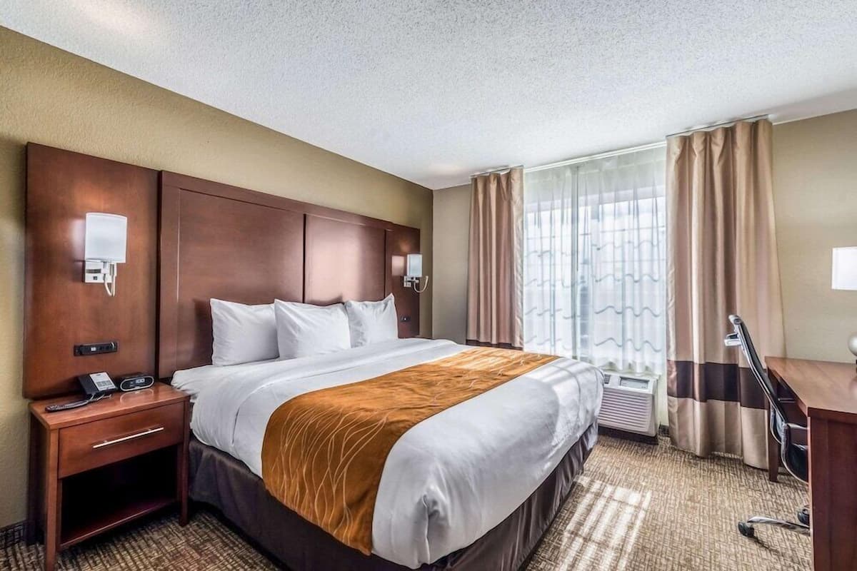 Une chambre d’hôtel avec un grand lit, des tables de chevet, un bureau et une fenêtre avec des rideaux.