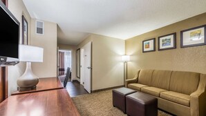 A hotel room with a wooden desk, a beige sofa, a flat-screen TV, and framed pictures on the wall. - Comfort Inn & Suites Dayton North (Dayton)