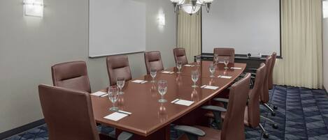 A conference room with a long table, brown leather chairs, a projector screen, and a chandelier.