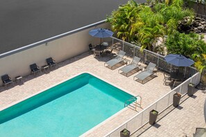 A rooftop pool area with a rectangular pool, lounge chairs, and umbrellas.