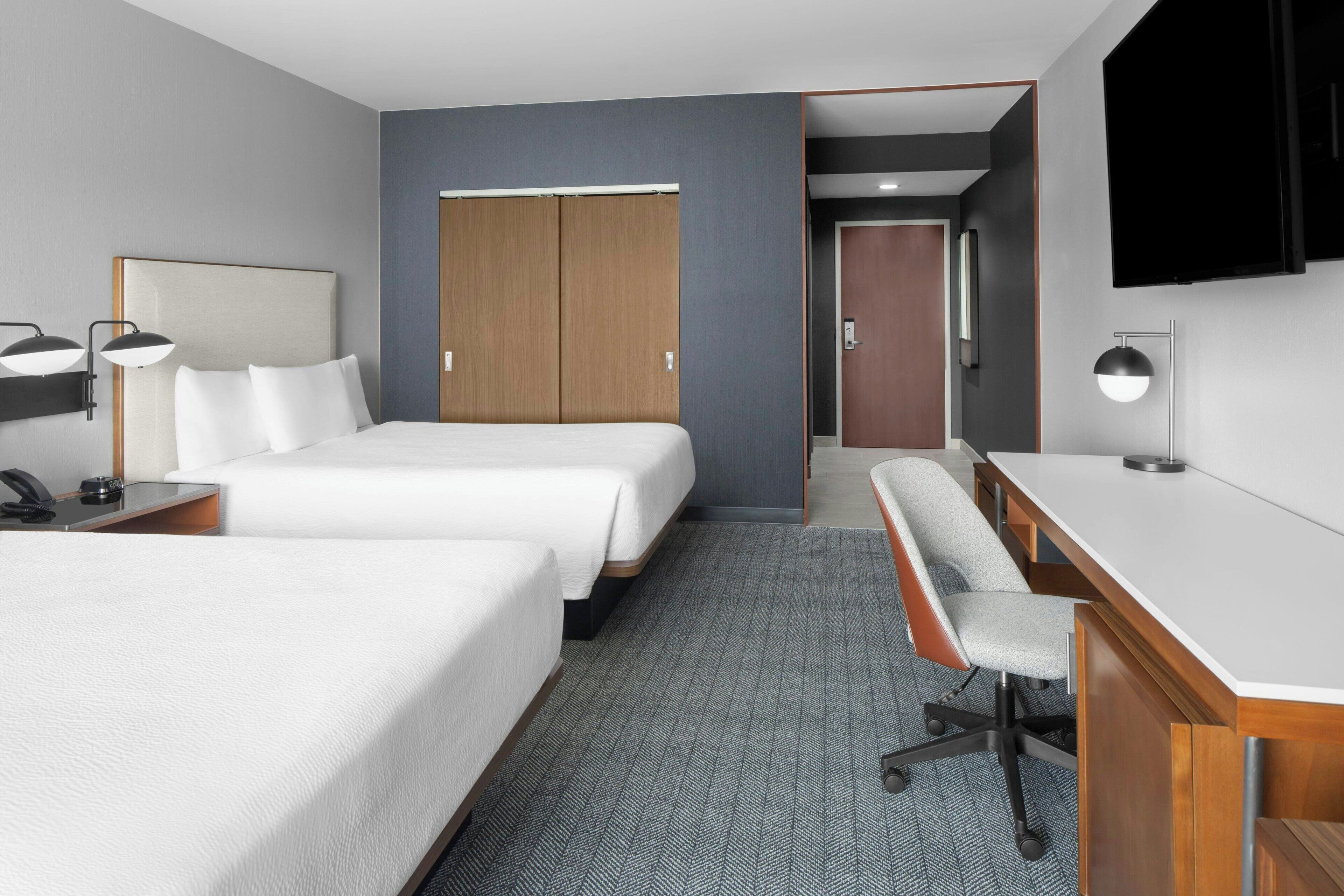 Habitación de hotel con dos camas, un escritorio, una silla, un televisor y un armario.