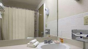 A bathroom with a white sink, a mirror, a towel rack, and a shower curtain. - Knights Inn Liberty (Liberty)