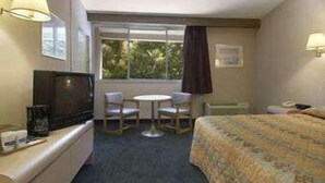 A hotel room with a bed, a desk, a chair, a television, and a window with a view of greenery. - Knights Inn Liberty (Liberty)