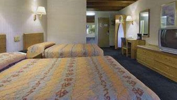 A hotel room with a bed, a dresser, a mirror, and a television. - Knights Inn Liberty (Liberty)