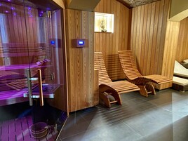 Una sauna con pareti in legno, una sauna in vetro e due lettini di legno.