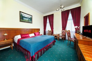 Una camera d'albergo con un letto, una scrivania con televisore, una sedia e un quadro appeso al muro.