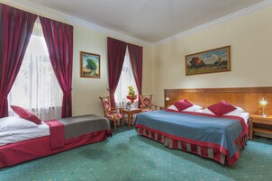 Una habitación de hotel con dos camas, un cabecero de madera, una mesita con un jarrón y un cuadro en la pared.