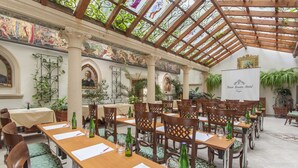 A spacious indoor dining area with long wooden tables and chairs, surrounded by potted plants and framed artwork. - Green Garden Hotel (Prague)