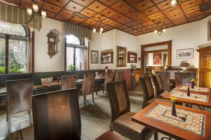 Een restaurant met houten tafels en stoelen, een klok aan de muur en uitzicht op het omliggende landschap.