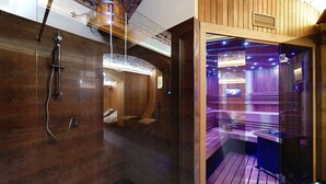A modern spa area with a wooden interior, a glass-enclosed shower, and a seating area with a television. - Green Garden Hotel (Prague)