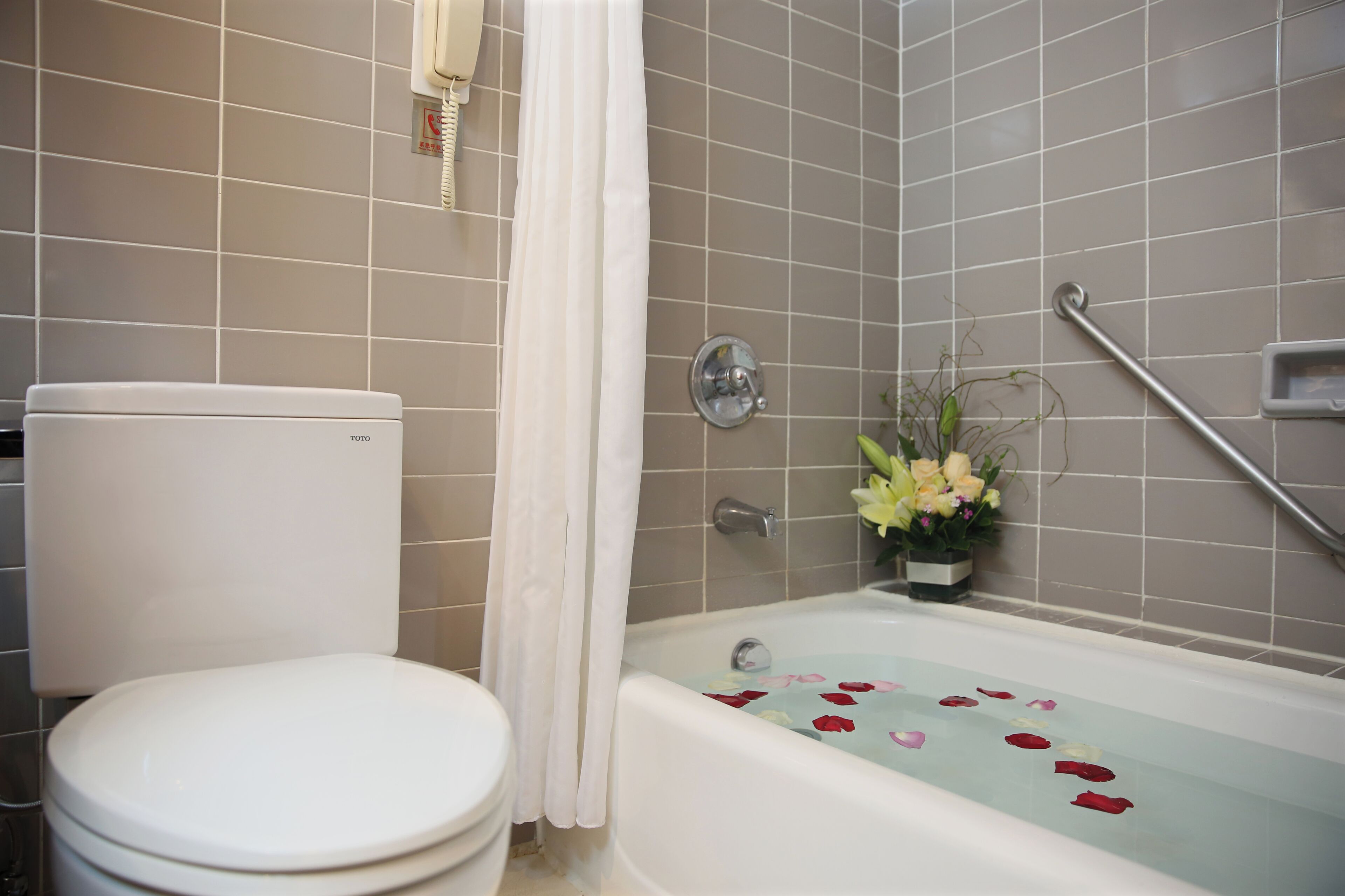 A bathroom with a toilet, a bathtub with rose petals, a shower curtain, and a handrail.