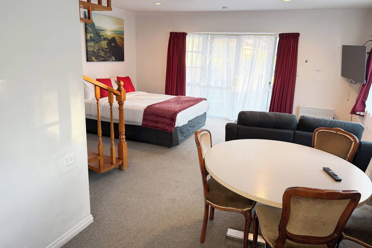 Ein Hotelzimmer mit einem Bett, einem Sofa, einem Esstisch mit Stühlen, einer Treppe und einem Bild an der Wand.