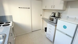 A kitchen with white cabinets, a stove, a microwave, and a refrigerator. - Settlers Motor Lodge (Lower Hutt)