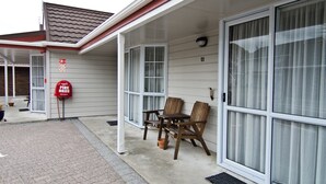 A covered outdoor area with a fire hose sign, two wooden chairs, and a door with a number 11 sign. - Settlers Motor Lodge (Lower Hutt)